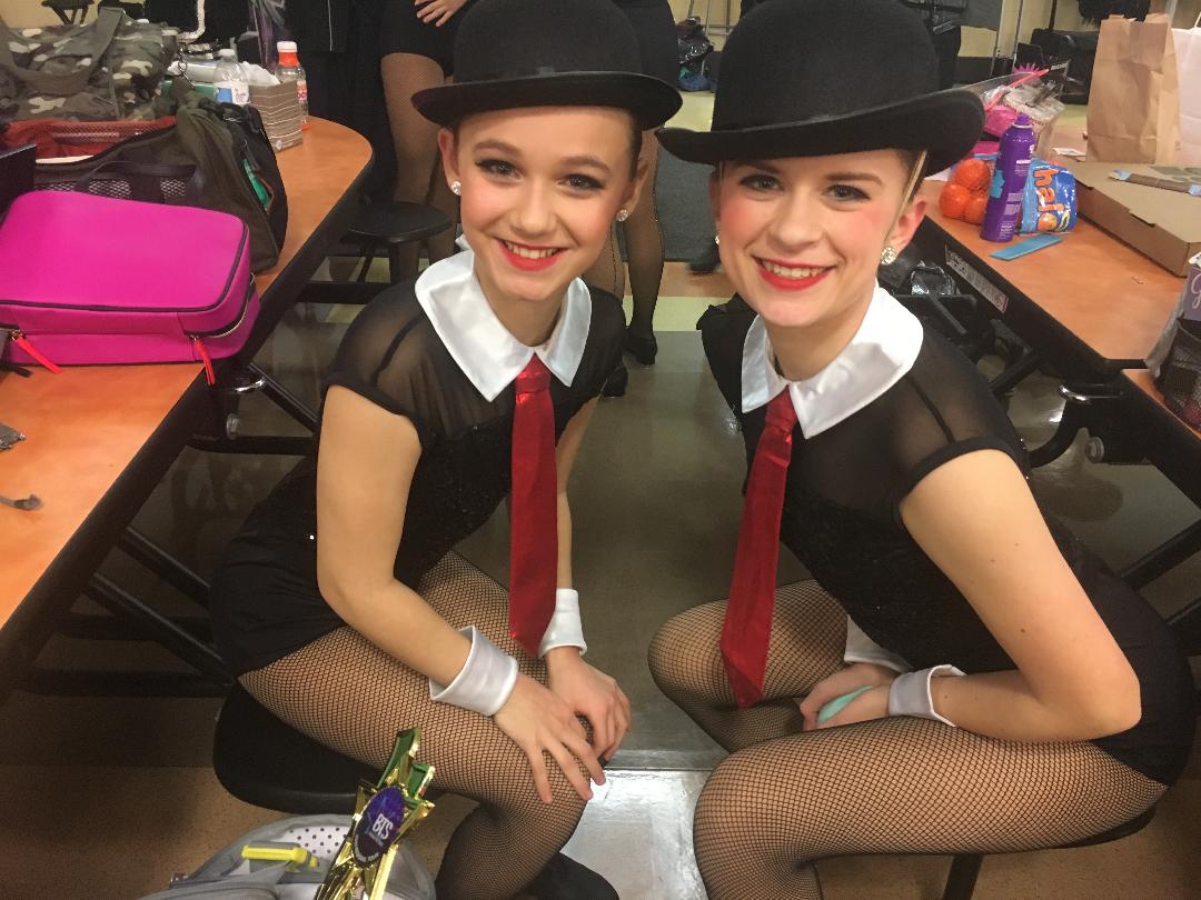 Two dancers in matching jazz performance costumes with hats and ties